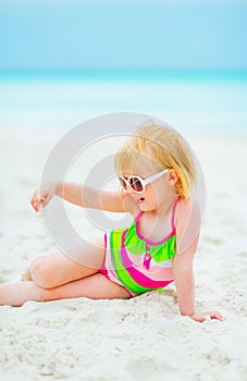 Baby girl in sunglasses playing with sand