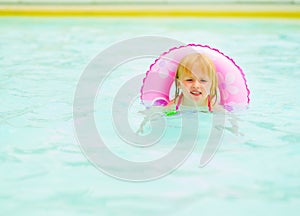 Baby girl with swim ring swimming in pool