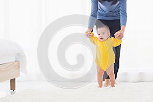 Baby girl taking first steps learning to walk with mom