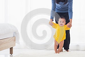 Baby girl taking first steps learning to walk with mom