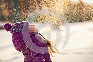 Baby girl throws the snow in frosty winter park. Flying Snowflakes. Sunny day. Child to have fun outdoors