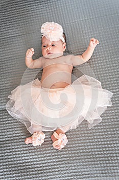 baby girl in tutu and pink ballet slippers lying on a gray blanket