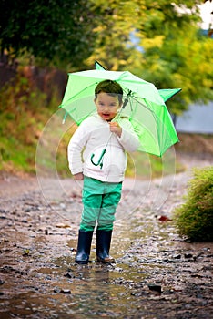Baby girl with an umbrella in the rain runs through the puddles