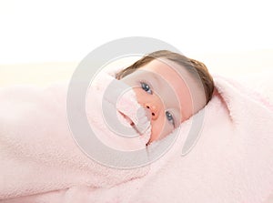 Baby girl under hidden pink blanket on white fur