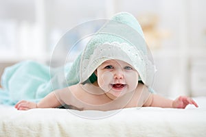 Baby girl under towel in bedroom after bath or shower. Textile and bedding for children.
