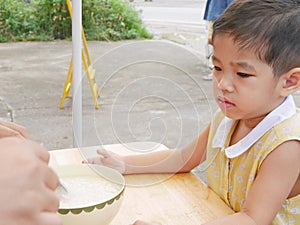 Baby girl with unhappy face unwilling to try new food, rice porridge