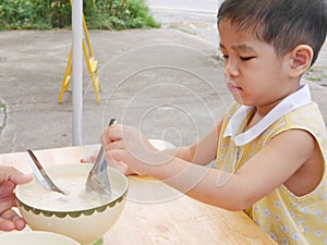 Baby girl with unhappy face unwilling to try new food, rice porridge