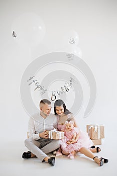 Baby girl unwrapping birthday present with happy parents