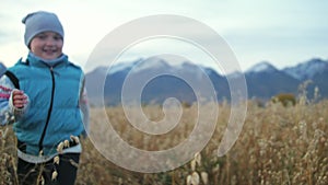 Baby girl walking in wheat field. Kid runs against the backdrop of beautiful mountains with snow capped peaks. Child