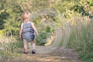 Baby girl walks away on green forest path