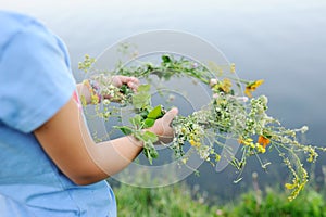 Baby girl walks on a river wreath of wild flowers