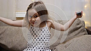 Baby girl watching TV. Child turns on the television using the remote.