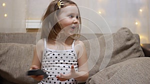 Baby girl watching TV. Child turns on the television using the remote.