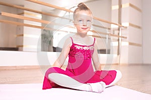 Baby girl wearing a peach tutu. a smiling baby girl is Sitting and stretching out on a sports mat