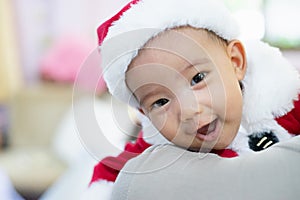 Baby girl wearing red Santa Claus costume she sit on father`s shoulder. she happy and smile.