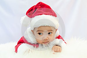 Baby girl wearing red Santa Claus costume sit on white fur carpet. Concept of celebrates Christmas and New Year
