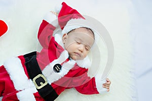 Baby girl wearing red Santa Claus costume sleep on white fur carpet. Concept of celebrates Christmas and New Year