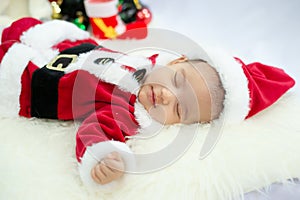 Baby girl wearing red Santa Claus costume sleep on white fur carpet. Concept of celebrates Christmas and New Year