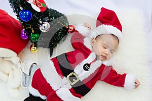 Baby girl wearing red Santa Claus costume sleep on white fur carpet. Concept of celebrates Christmas and New Year