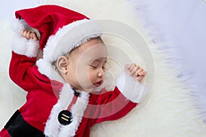 Baby girl wearing red Santa Claus costume sleep on white fur carpet. Concept of celebrates Christmas and New Year