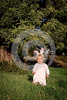 Baby girl wears rabbit ears, sitting in grass