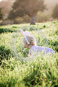 Baby girl wears rabbit ears, sitting in grass