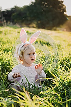 Baby girl wears rabbit ears, sitting in grass