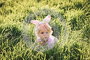 Baby girl wears rabbit ears, sitting in grass