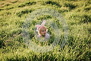 Baby girl wears rabbit ears, sitting in grass