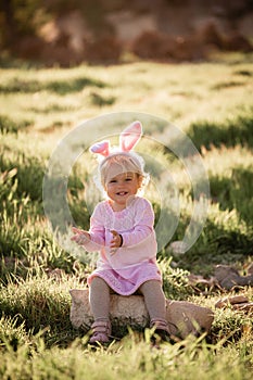 Baby girl wears rabbit ears, sitting in grass