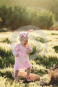 Baby girl wears rabbit ears, walking in grass