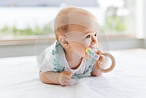 Baby girl on white blanket chewing wooden rattle