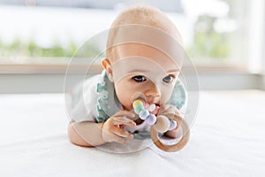 Baby girl on white blanket chewing wooden rattle