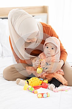 Baby girl  in the white hijab toddler clothes playing toy with her mother