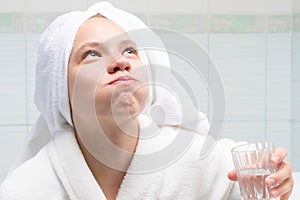 Baby girl, in a white robe and towel on her head, in the bathroom, holding a glass of water and rinsing her mouth, after cleaning