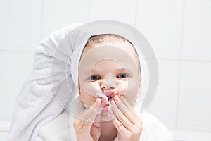 Baby girl, with a white towel on her head, cleans her lips with a round cotton swab, after lipstick, close-up, on the background