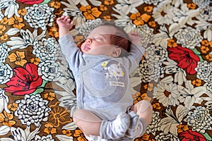 Baby with grey body asleep on a sheet with flower print