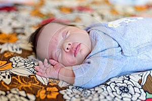 Baby with grey body asleep on a sheet with flower print