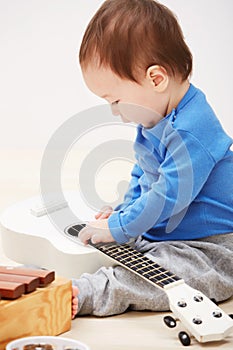Baby, guitar toys and play in home for entertainment joy, childhood development or education. Boy, kid and instruments