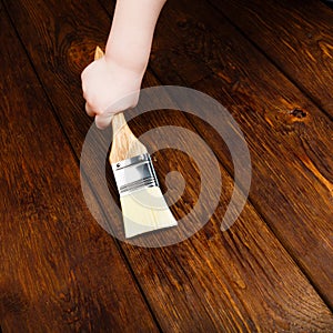 Baby hand applying protective varnish on a wooden table