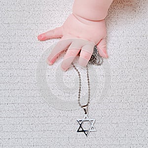 Baby hand and Jewish religious symbol is the star of David, close-up. Children fingers and an object on a white background