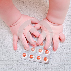 Baby hand and medicines tablets in a package, close-up. Children fingers and an object on a white background