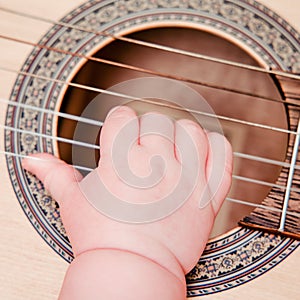 Baby hand and musical instrument guitar, close-up. Children fingers and an object on a white background