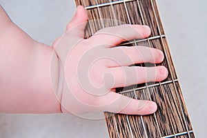 Baby hand and musical instrument guitar, close-up. Children fingers and an object on a white background