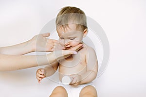 Baby handling: Woman applying moisturizing cream on her baby`s face. The baby holds the tube with a cream in her hands