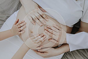 Baby hands hold the belly of a pregnant mom.