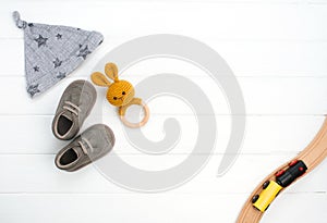 Baby hat, booties and wooden teether and train toy on white wooden background