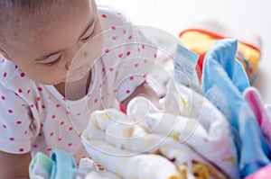 Baby with heap of colorful clothes in the room