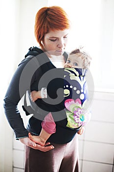 Baby held by his mother in a baby carrier photo