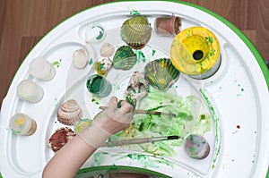 Baby and her father painting together. Kid diping her finger in paint. Hands with a brush painting the shells.